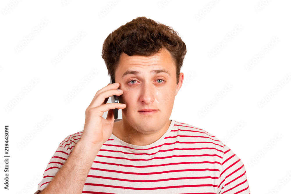 A young man cries about bad news by closing his eyes and thinking about the problem that he gets on his phone. emotional man isolated on white background A young man cries about bad news by closing his eyes and thinking about the problem that he gets on his phone. emotional man isolated on white background