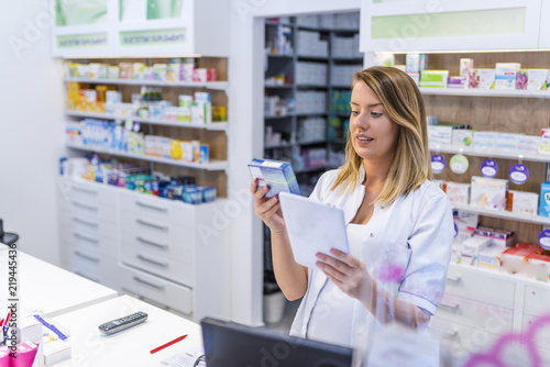  Young pharmacist holding a tablet and box of medications.