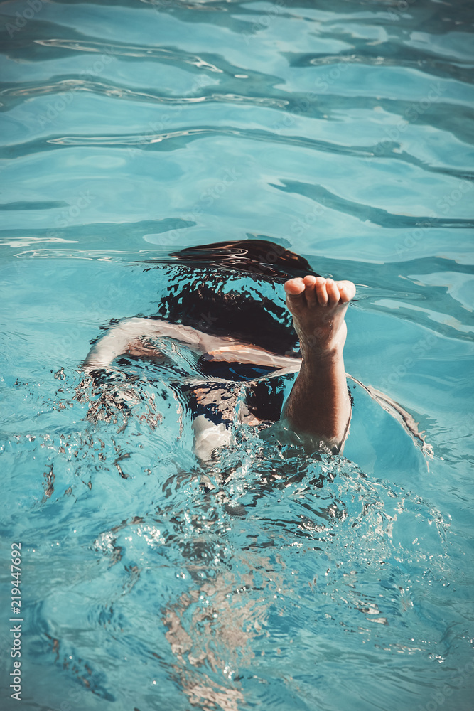 Young girl in the swimming pool diving under and making some acrobatics. Close up of foot, body parts.