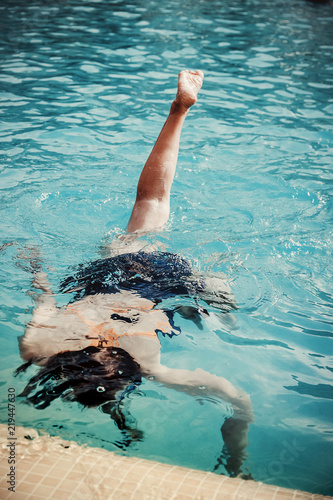 Young girl in the swimming pool diving under and making some acrobatics. Close up of foot, body parts.