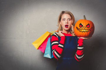 Young style girl in jeans clothes with shopping bags and halloween pumpkin on grey background.