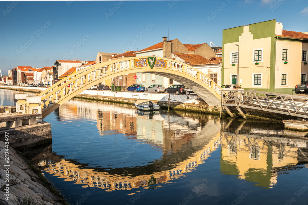 Carcavelos bridge on the São Roque canal, in the city of Aveiro, Portugal, with houses in the background and reflection in the water.