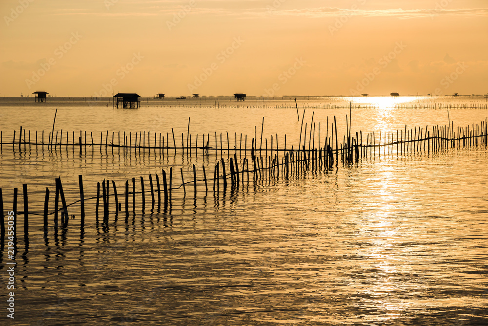 Traditional fisherman sea mussel farming and wooden house along the sea coast with golden sunrise sky background, livelihoods of fishermen in Thailand