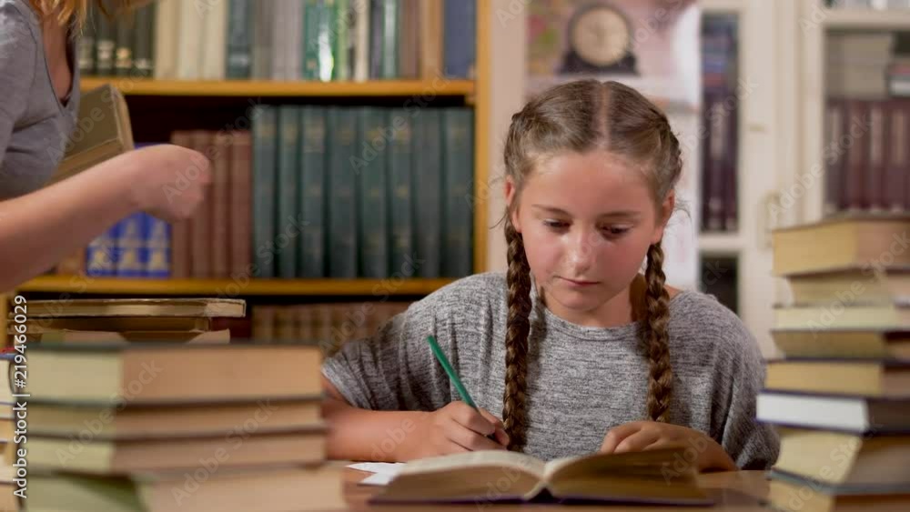 Little girl writes at a table in the library Little girl writes at a table in the library