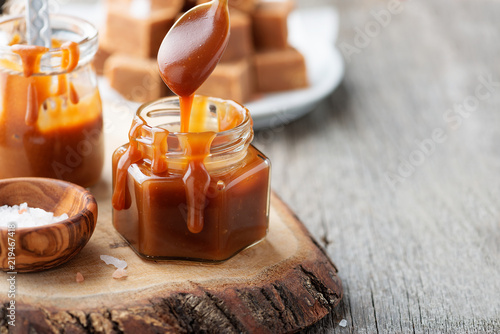 Homemade salted caramel sauce in jar on rustic wooden table. photo