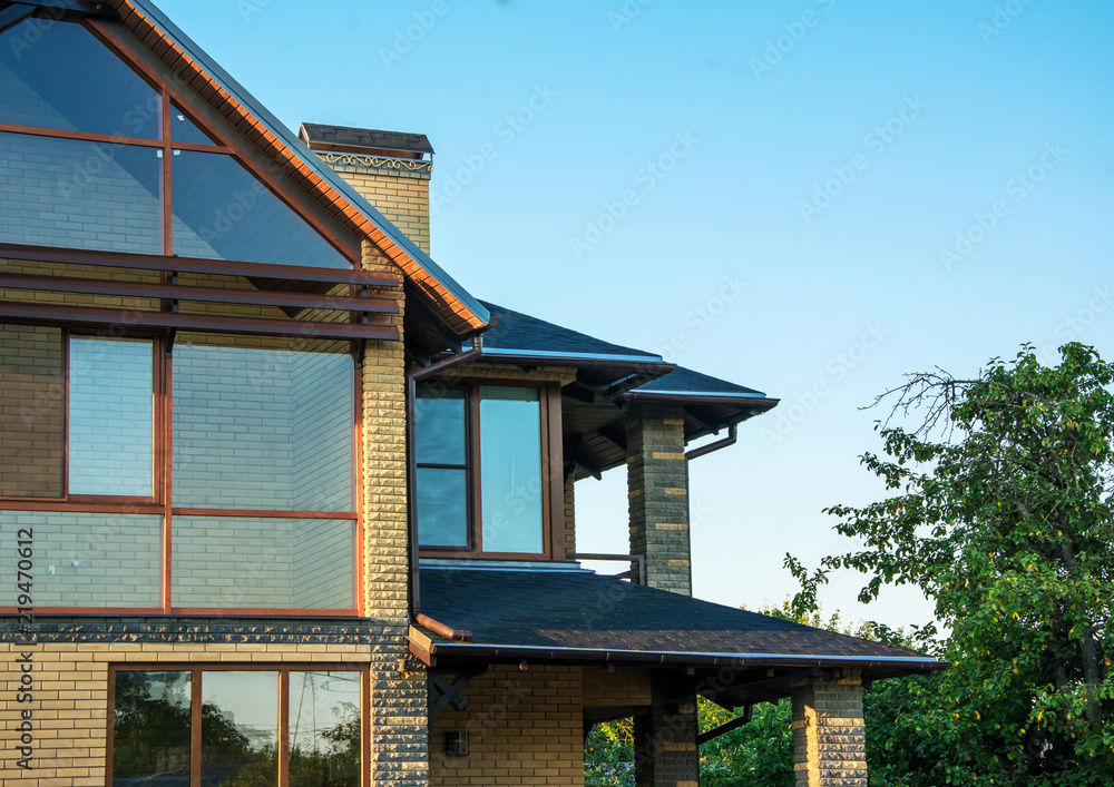 Brick house with panoramic windows, multilevel roof, glazed facade, chimney with forging, closeup.