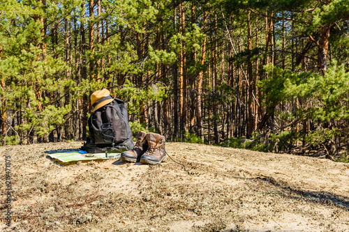 Backpack, touristic boots, map, compass and hat on a ground in a coniferous forest