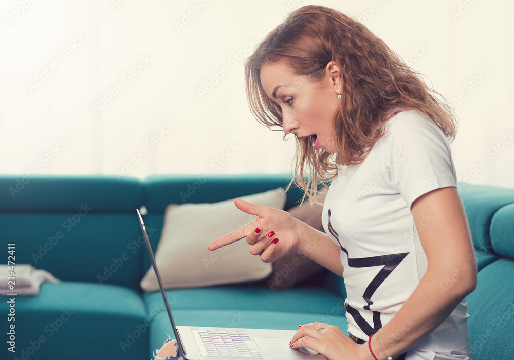 Portrait of an amazed surprised woman with laptop sitting on a couch Portrait of an amazed surprised woman with laptop sitting on a couch
