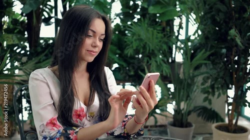 Wallpaper Mural Young brunette woman in summer cafe web surfing with her pink smartphone. Left to right pan slow motion medium shot Torontodigital.ca