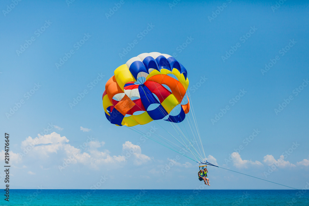 Couple of tourists flying on a colorful parachute Couple of tourists flying on a colorful parachute