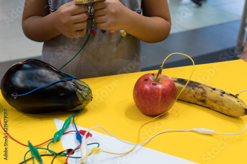 Fruit piano with kids. STEM education activity allow kids to play music with fruit and vegetables. Microcontroller converts keys in sound with some fruits. Yellow background and vegetables wired photo