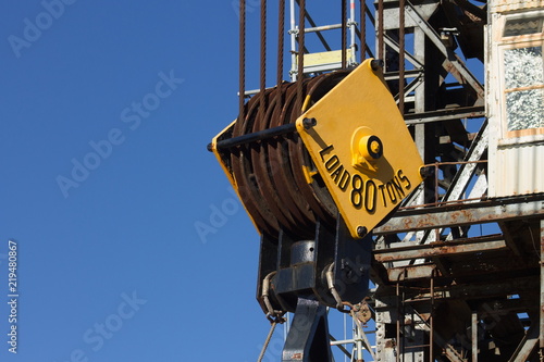 Close up image of a steel cable pulley on a crane against a blue sky.