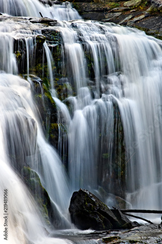 Mountain waterfall dropping over smooth moss rocks in blurred motion.