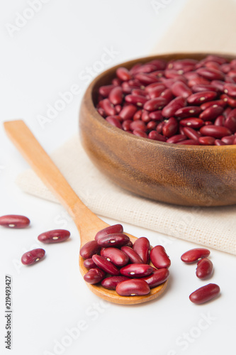 Red beans in wooden bowl and spoon putting on linen and white background.