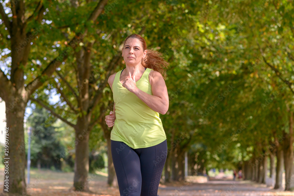 Fit middle-aged woman jogging through a park Fit middle-aged woman jogging through a park