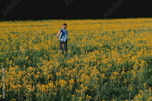 Boy runs on the field among the yellow flowers.