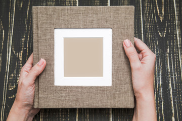 Top view photography of new brown modern photo book with empty frame for photo. White woman holds album with love. Isolated on wooden background. Horizontal color picture.