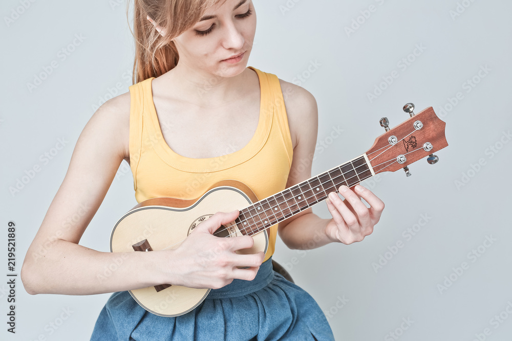 Fototapeta premium Attractive woman with light hair plays ukulele on white background