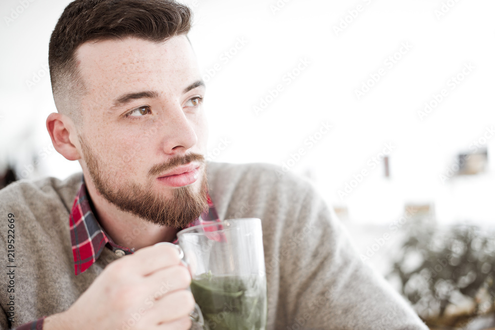 Young handsome hipster man with cup of mint tea sitting in the room in cafe Young handsome hipster man with cup of mint tea sitting in the room in cafe
