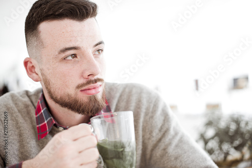 Young handsome hipster man with cup of mint tea sitting in the room in cafe