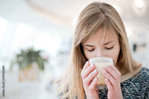 Woman holding cup of hot coffee drink in her hands with french stylish manicure, sitting in the room in warm cozy sweater