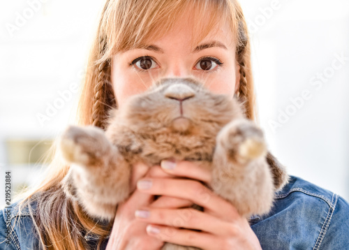 Young woman hugs big cute rabbit friend pet in her hands. Funny portrait with bunny