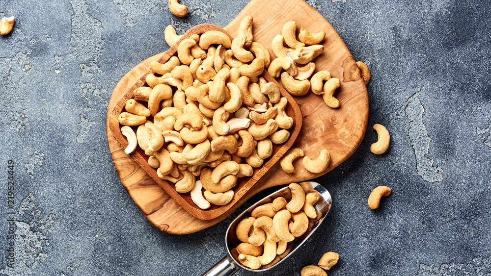 Fototapeta premium Roasted cashew nuts and scoop on gray background. Top view.