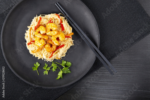 Fried prawns and rice noodles with spices on a black plate. The background is black. Top view. Eastern food. Copy space.