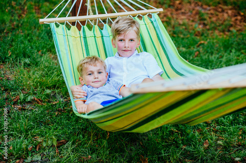 Two happy blond scandinavian children swinging and relaxing In garden hammock together.