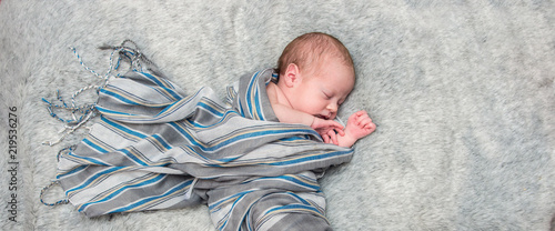  sleeping infant baby boy on a wrapped in a gray scarf on a gray furry bedspread