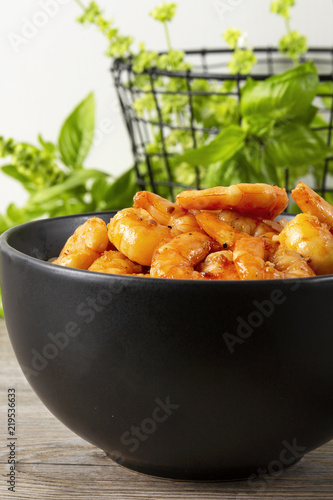 Fried shrimps in a black bowl. On a background basket with greens. Eastern food.