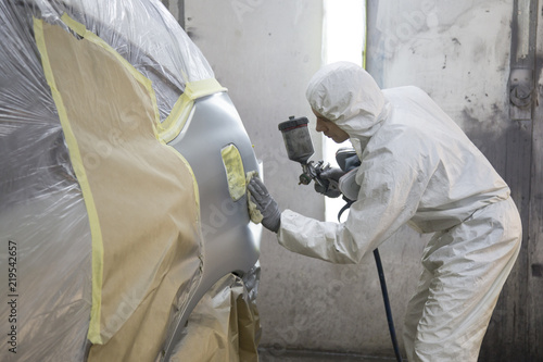 auto mechanic worker painting car in a paint chamber during repair work