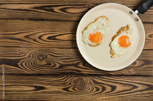 Two fried eggs in metal beige pan on old wooden brown table. Top view and copy space