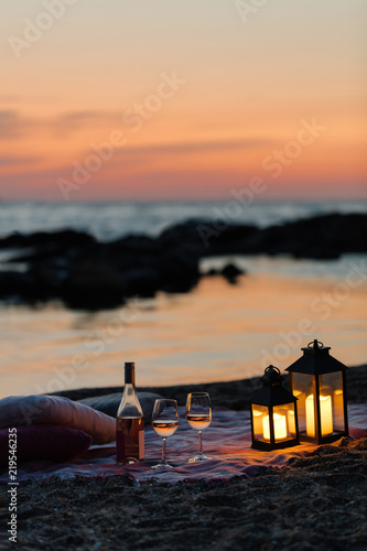Summer sea sunset. Romantic picnic on the beach. Bottle of wine, glasses, candles, plaid and pillows.