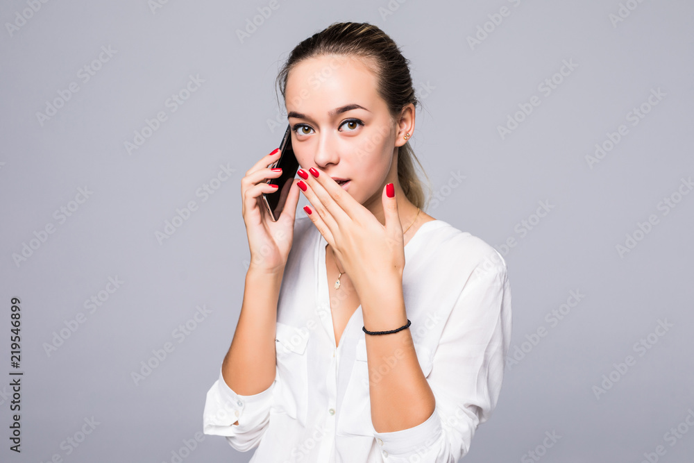 Portrait of surprised and impressed woman with widened eyes and opened mouth, stunned because of something she is hearingin phone while standing against gray background. Portrait of surprised and impressed woman with widened eyes and opened mouth, stunned because of something she is hearingin phone while standing against gray background.