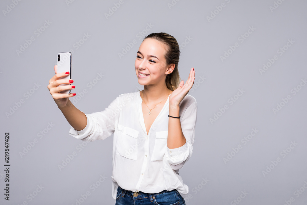Sociable beautiful woman taking selfie or speaking on video call using cell phone isolated over gray background Sociable beautiful woman taking selfie or speaking on video call using cell phone isolated over gray background