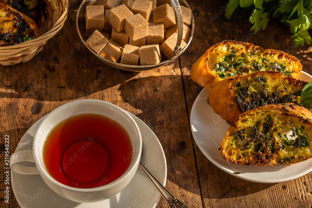 Lunch - tea and traditional French baguette toast with butter, parsley, garlic and basil on an old rustic wooden table Lunch - tea and traditional French baguette toast with butter, parsley, garlic and basil on an old rustic wooden table