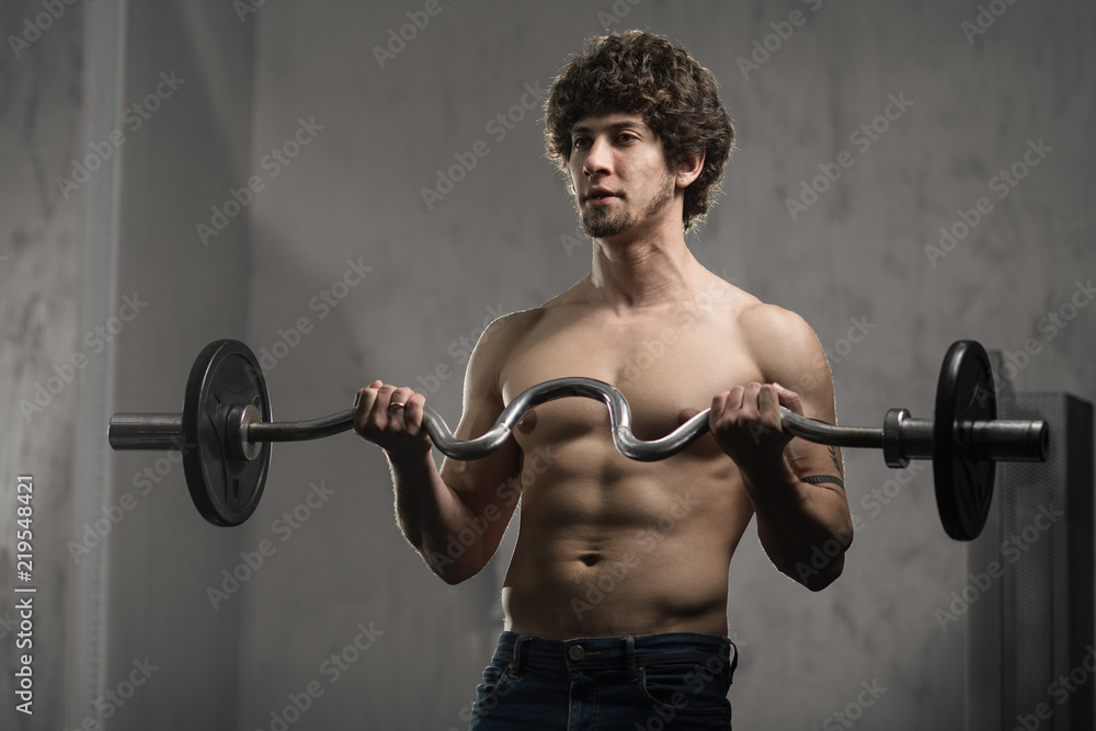 Muscular man trains biceps with barbell in the gym, hand training Muscular man trains biceps with barbell in the gym, hand training