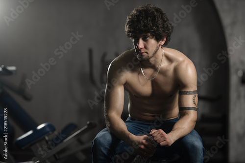 Young attractive man resting in gym after exercising, male posing