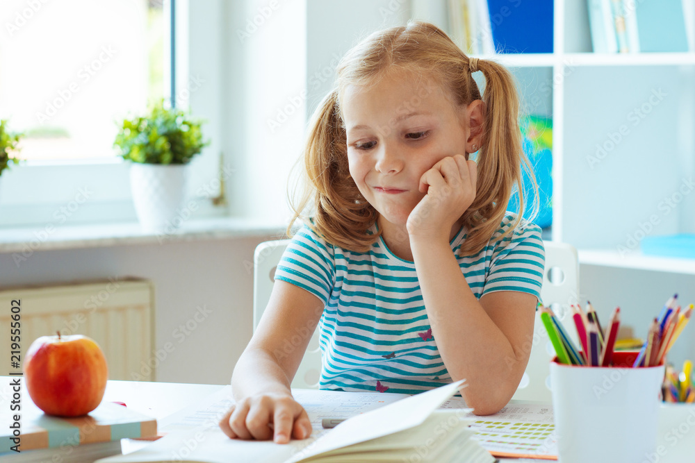Portrait of a thoughtful cute girl sitting at a table with books in a light classкroom Portrait of a thoughtful cute girl sitting at a table with books in a light classкroom