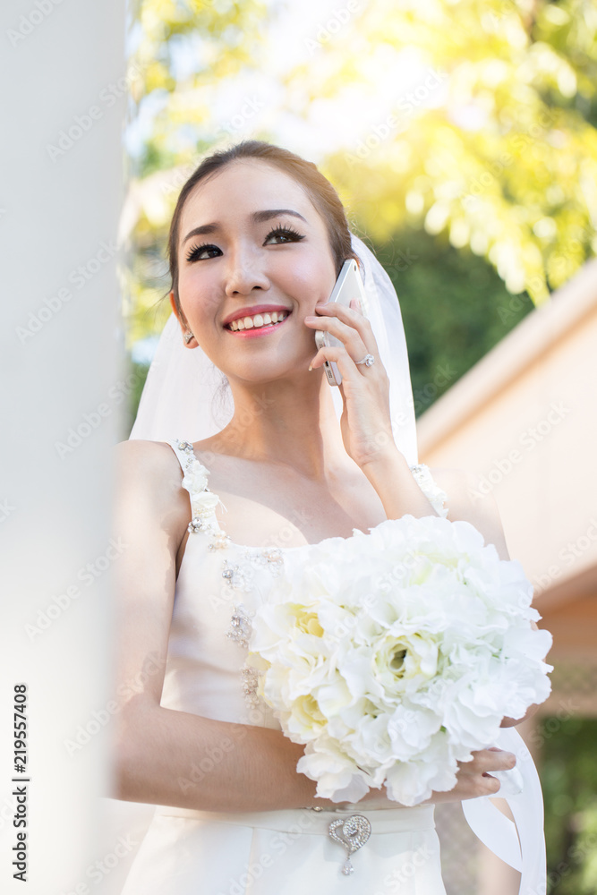 Beautiful Attractive Asian bride talking with her friend in smartphone in wedding day feeling so proud and happiness Beautiful Attractive Asian bride talking with her friend in smartphone in wedding day feeling so proud and happiness