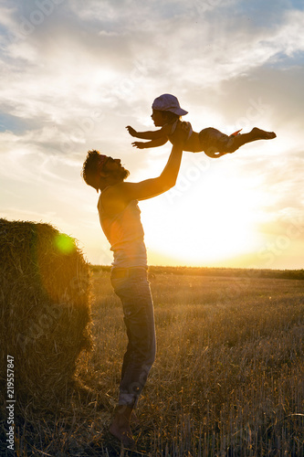 father throws his son into the sky next to a haystack