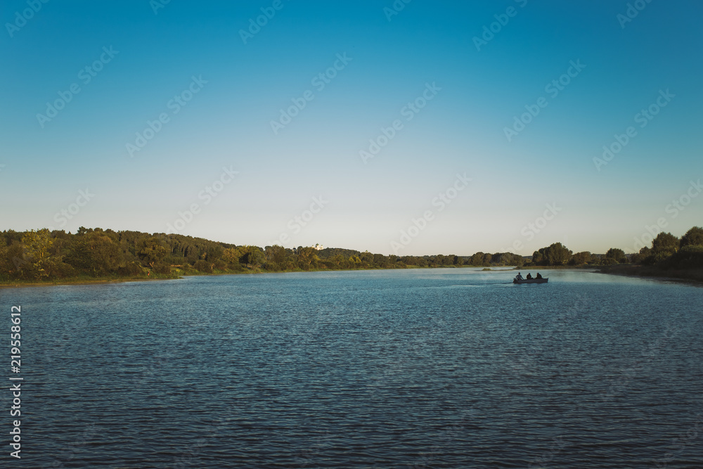 Beautiful morning river landscape with silhouette of traditional wooden boat and three men sitting in it with fishing rods. Happy vacation concept. horizontal color photography.