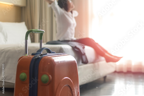 Work and business travel concept. Baggage or luggage of businesswoman arrive in hotel room and woman sit on bed. © Khunatorn