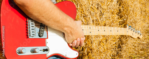 Guitar telecaster in red with a wooden stamp in the hand of a musician background of straw on a sunny summer day