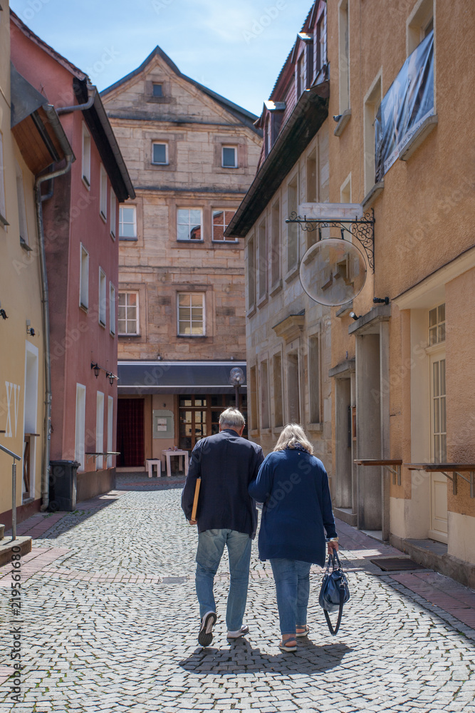 An elderly couple in love walks along an old German cobblestone street