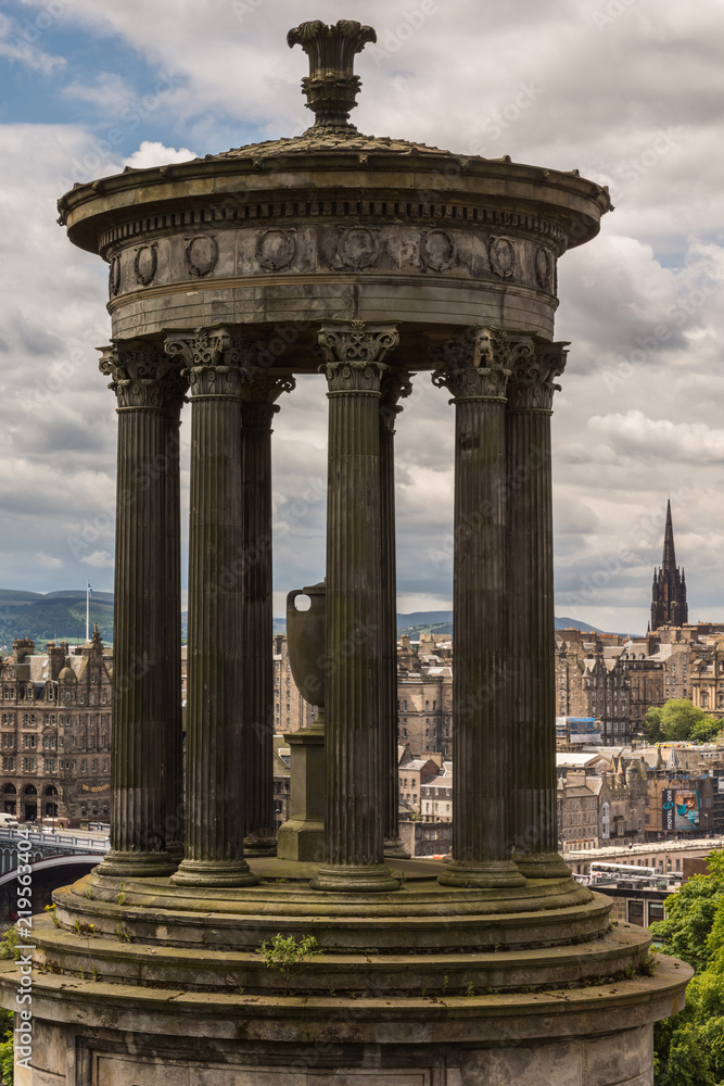 Edinburgh, Scotland, UK - June 13, 2012: Closeup of brown stone Donald Stewart Monument on Calton Hill. Background is buildings of Old Town. All under heavy cloudscape.