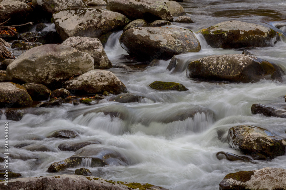 Stream with touches of blue reflections, fall leaves, water flowing over rocks, horizontal aspect Stream with touches of blue reflections, fall leaves, water flowing over rocks, horizontal aspect