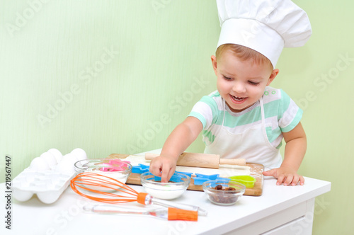 Cheerful cute baby boy in a chef costume smiling standing at the table where doing cookies