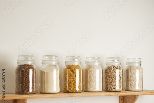 Various uncooked cereals, grains, pasta, bukwheat, rice, oat meals. Healthy cooking in glass jars on wooden table. Balanced dieting food. Copy space.